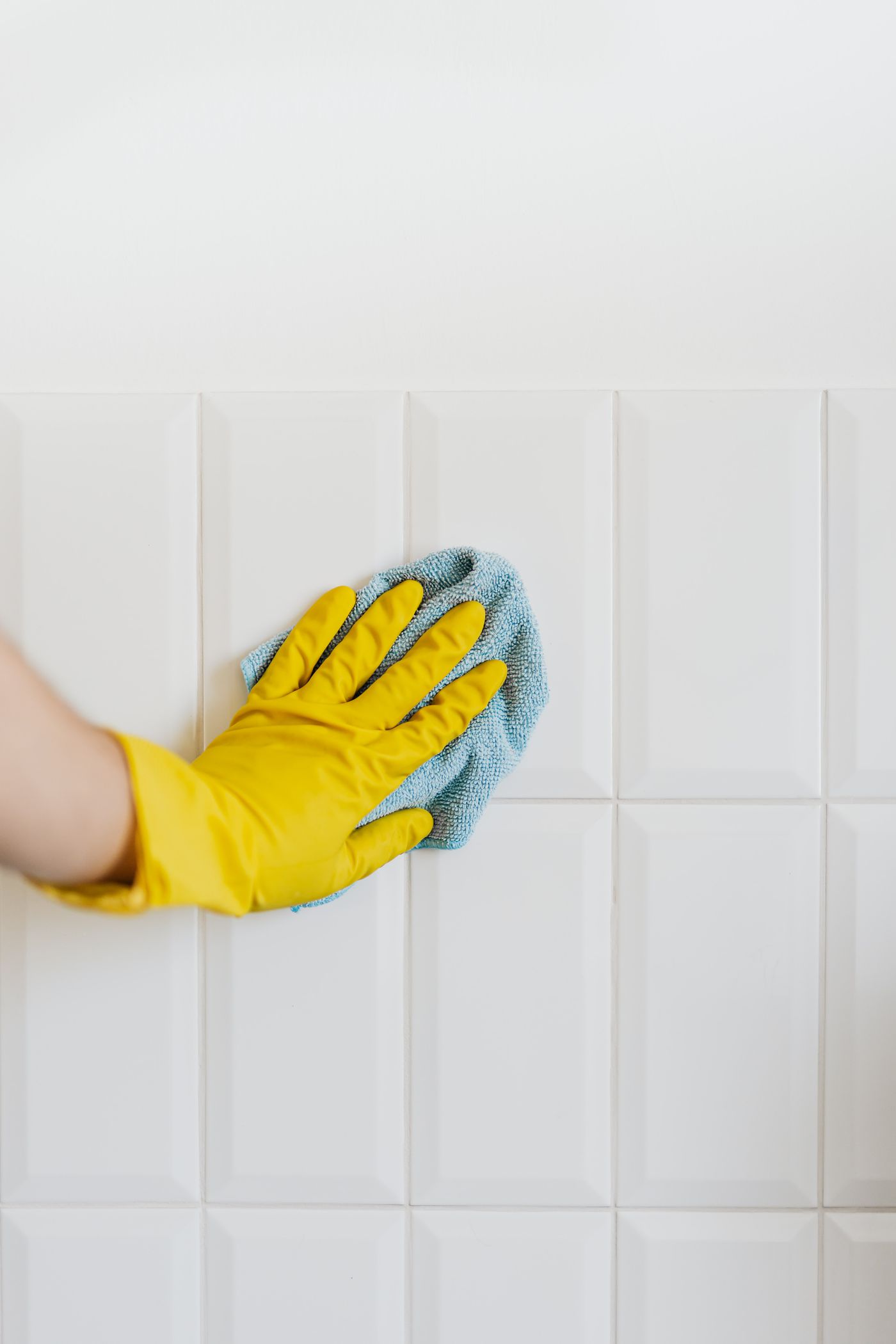 Mano con guante amarillo limpiando azulejos con un paño de microfibra